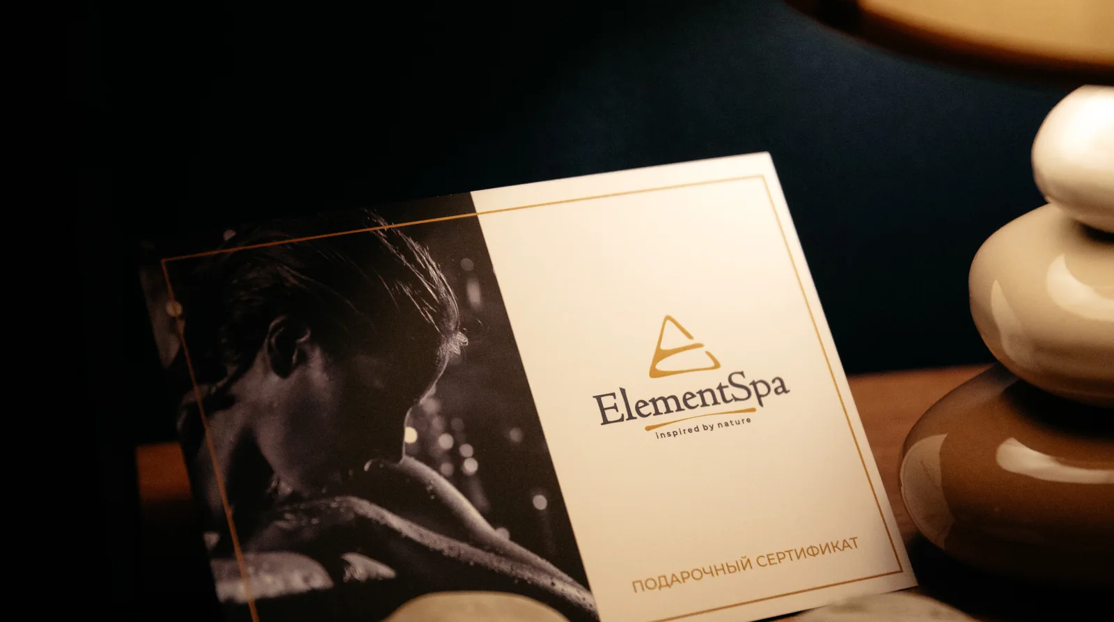 Подарочный сертификат Element Spa на деревянном столе у настольной лампы